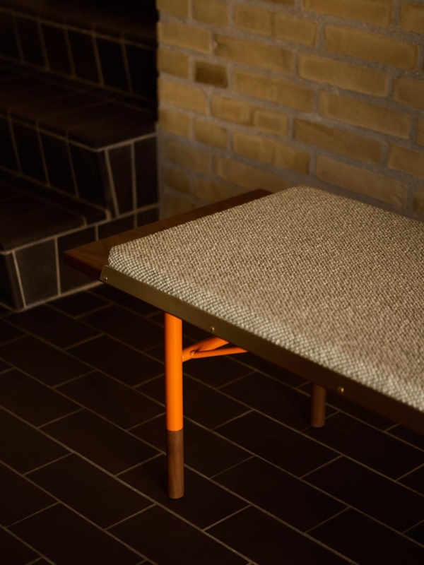 The Table Bench in walnut with orange steel legs and brass edges. Cushion with 'Safire' upholstery in the colour '0006'.